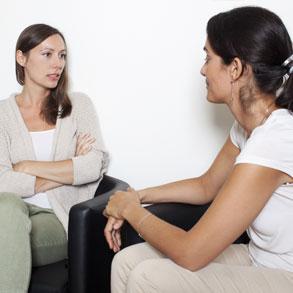 A woman sits defensively while receiving support from another woman